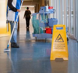 Cleaning the floor with a mop. House keeping. Sign take care slippery.