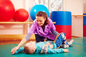 cute kid with disability has musculoskeletal therapy by doing exercises in body fixing belts