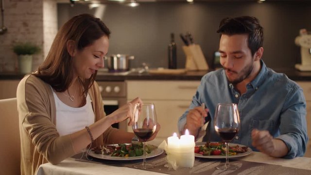 Beautiful Couple Having Candlelight Dinner in the Kitchen. They Eat, Drinl and Talk. Both are in Good Mood and Smile a lot. Slom Motion. Shot on RED Cinema Camera in 4K (UHD).