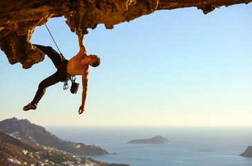 Young man climbing on roof of cave against view of coast