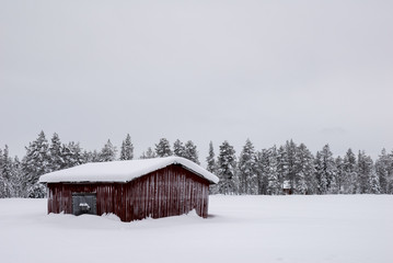 Barn under a grey winter sky and deep snow in Lapland, Finland
