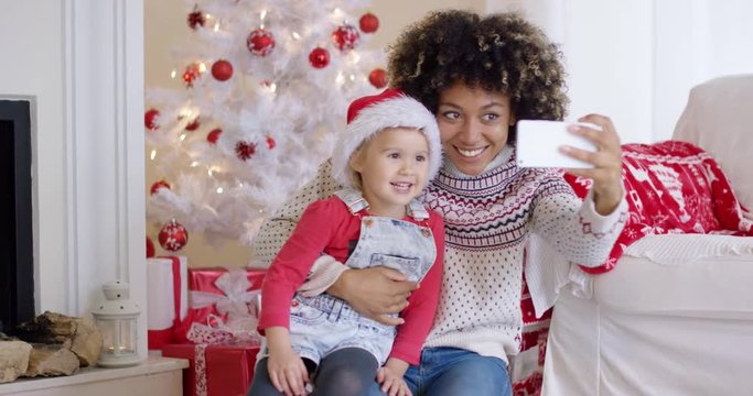 Woman and child posing for camera phone in front of white Christmas tree decorated with red ornaments