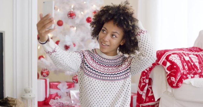 Young woman posing for a Christmas selfie in a red and white themed living room with decorated tree