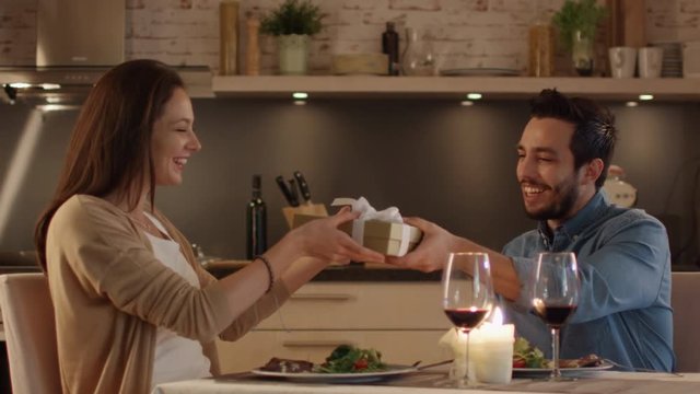 Couple Having Romantic Dinner. Handsome Man Gives His Girlfreind a Gift Box. She Bemusedly Accepts.   Shot on RED Cinema Camera in 4K (UHD).