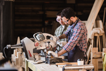 Two carpenters cutting wooden plank with a circular saw