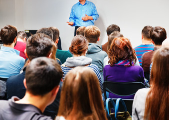 Speaker explain essence method with hand-play gesticulation, group of people students are listening attentively, romantic couple of students at foreground.