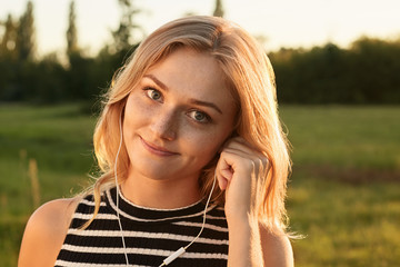 A nice-looking girl with magic smile looking straightly in the camera and listening to the music with her earphones. A girl touching her earphones with her hand. © sementsova321