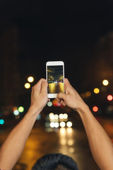 Boy takes a photograph of a street at night.