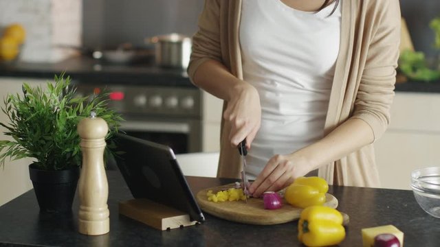 Close-up of a Woman Cutting Vegetables on the Wooden Board. Consulting Her Tablet Computer for Recipe. Shot on RED Cinema Camera in 4K (UHD).