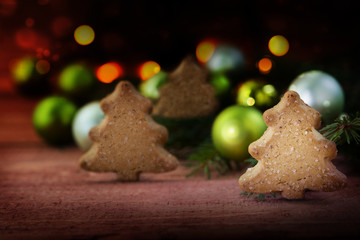 Small forest of christmas cookies in tree shape, spruce branches and baubles, dark background