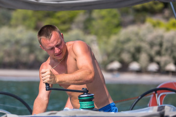 Young male sailor turns of the rope on the yacht boat.
