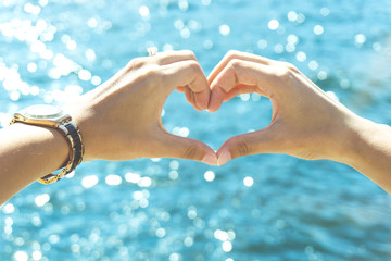 Female hands in love heart shape with the blue sea in the background - Harmony, feelings and emotions

