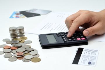 A business man hand using the calculator with coin stacks and financial report on the table 