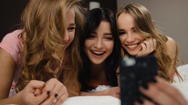 Three beautiful smiling curly friends with similar nails taking selfies on the bed.