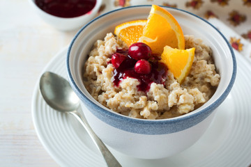  Oat porridge with cranberry sauce and orange in a ceramic bowl for healthy breakfast on a light background. Selective focus.
