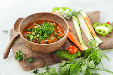 Vegetarian soup in wooden bowl on wood board on white table
