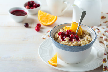  Oat porridge with cranberry sauce and orange in a ceramic bowl for healthy breakfast on a light background. Selective focus.