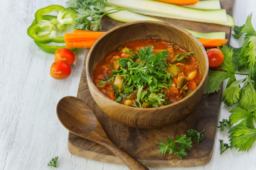 Vegetarian soup in wooden bowl on wood board on white table