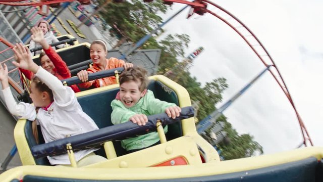 Happy kids yelling, raising arms and waving while riding roller coaster in amusement park