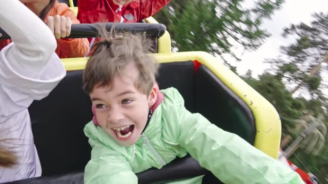 POV shot of excited children shouting and raising arms while riding roller coaster in amusement park