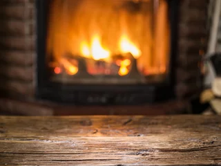 Fotobehang Old wooden table and fireplace with warm fire on the background. © volff