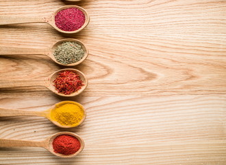 Assortment of colorful spices in the wooden spoons on the wooden