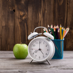 Retro alarm clock with colored pencils and green apple