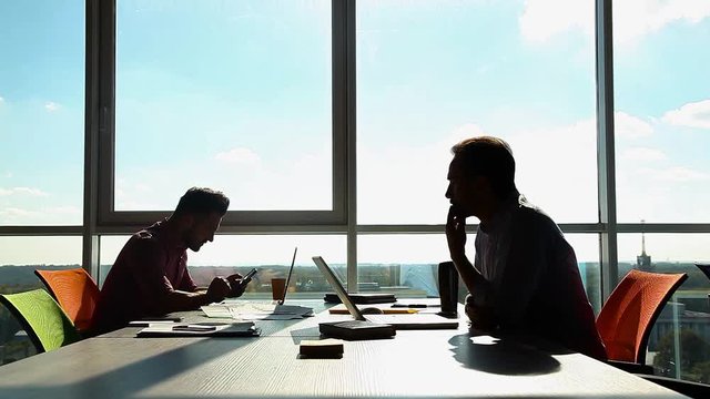 Two businessmen working in office while sitting at table in boad room. One man usinf mobile or smart phone, another taking document. Business concept.