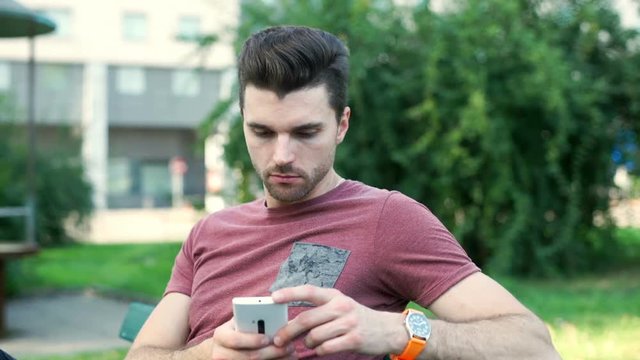 Calm man sitting on the bench and browsing internet on smartphone
