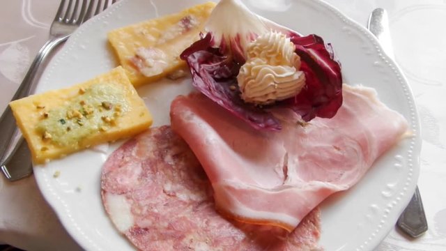Plate with typical italian starters: cold cuts as coppa and prosciutto, pesto sauce with nuts on fried polenta slices and mascarpone mousse on Treviso chicory.