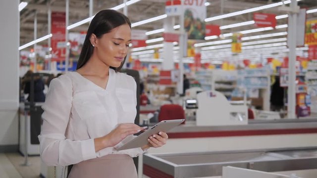 Happy Woman with Tablet Shopping at The Supermarket - Young girl in a market store with a PC tablet in a department store