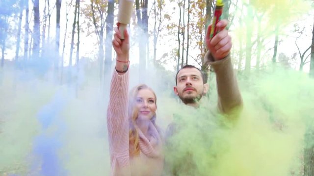 Man and woman kissing and holding bright yellow and purple smoke. In the forest