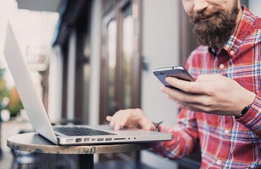 Young man texting on his smartphone and using laptop computer on an urban background