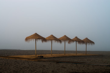 Playa con bruma y sombrillas de paja