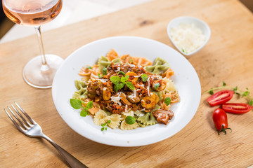 Farfalle with meat, mushrooms, olives and basil on a classic wood. Rose wine glass and dishes.