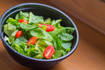 Organic mixed green salad in a transparent plastic plates on  wooden table very tasty