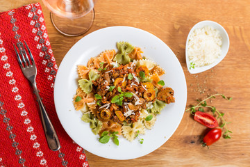 Italian pasta Farfalle with meat, olives, basil and mushrooms. Rose wine glass visible. Top view.