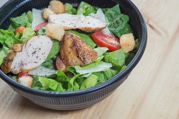 Organic mixed green salad with chicken in a transparent plastic plates on  wooden table very tasty