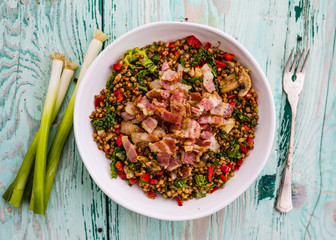 Buckwheat with bacon and vegetables served on white plate. 