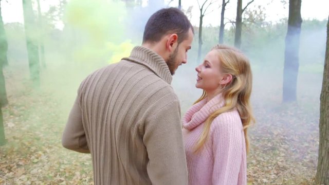 Man and woman kissing and holding bright yellow and purple smoke. In the forest