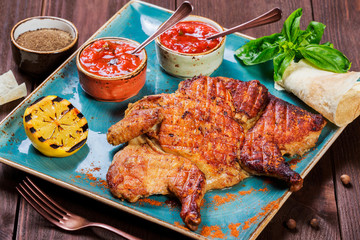 Roasted Chicken or turkey with spices, lemon, tomato sauce, basil and pita bread on plate on dark wooden background. Thanksgiving table served with knife and fork. Top view