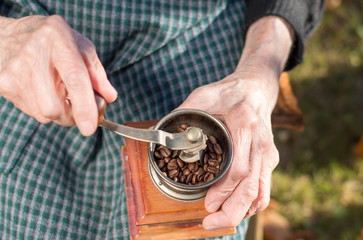 Old woman grinding coffee on a vintage coffee grinder