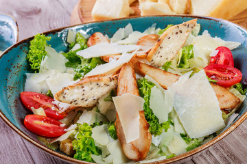 Salad with chicken breast, parmesan cheese, croutons, tomatoes, mixed greens, lettuce and glass of wine on light wooden background. Ingredients on table