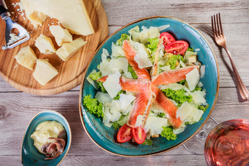 Salmon salad with tuna sauce, parmesan cheese, croutons, tomatoes, mixed greens, lettuce and glass of wine on wooden background. Mediterranean food. Top view