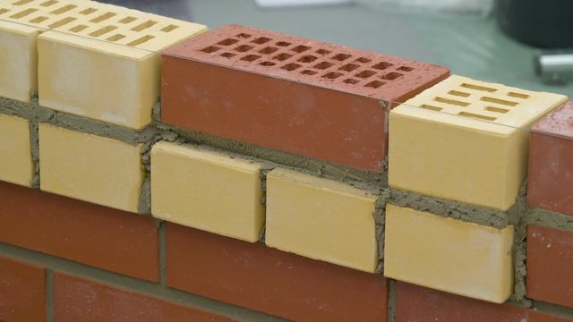 A man using a ruler to make sure the bricks are aligned then filling up cement in between each bricks