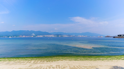 Fototapeta premium Scenery of sea coast on Miyajima Island where Itsukushima shrine located viewing ferry terminal , activities in the bay and Hiroshima city in the background , Japan