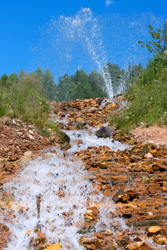 Waterfall and geyser in sunny day.