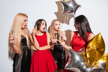 Surprised young women drinking champagne and talking on the party
