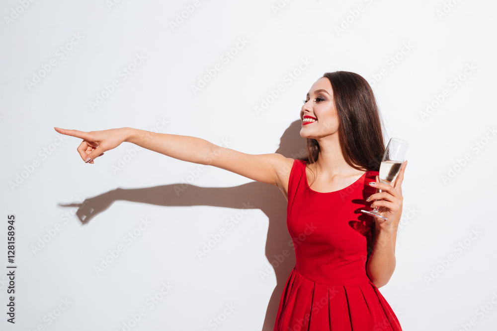 Sticker Smiling woman in red dress drinking champagne and pointing away