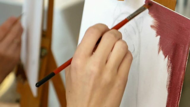 Female artist paints a picture oil painting artwork drawing on canvas easel in art studio. Student girl learning to draw and paint.